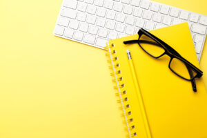 Student or freelancer workspace with keyboard, glasses, notepad, pencil on yellow background, flat lay. Space for text