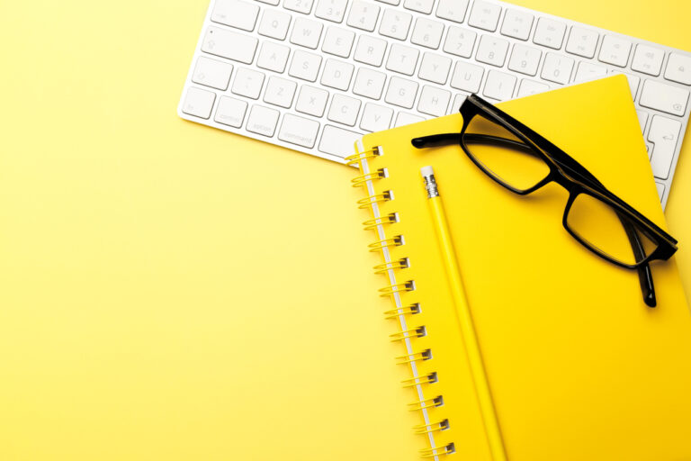 Student or freelancer workspace with keyboard, glasses, notepad, pencil on yellow background, flat lay. Space for text