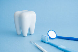 White healthy tooth model, dental pick explorer probe, blue toothbrush and dentist mirror on blue background with copy space. Dental care and healthcare concept.