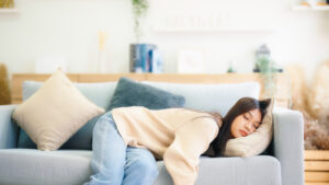 Asian woman resting at home on couch, feeling exhausted after work, lacking energy, or overworked, too tired, and lacking motivation