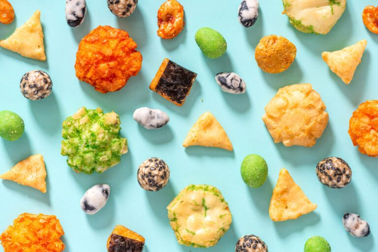 Pattern from various Japanese snacks on a blue background. Top view, flat lay. Rice crackers with wasabi and nori, peanuts with sesame seeds, and other snacks. Mix traditional Japanese snack food.